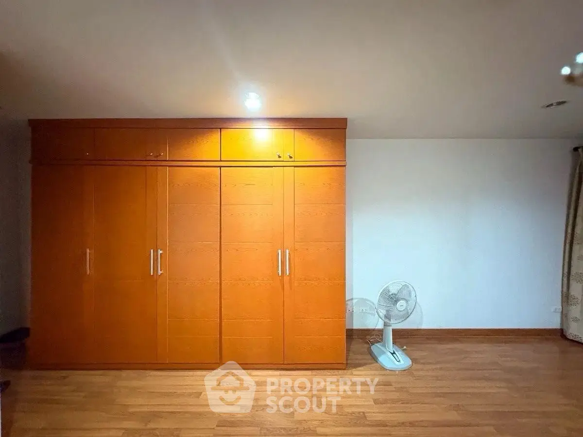 Spacious bedroom with wooden wardrobe and floor fan