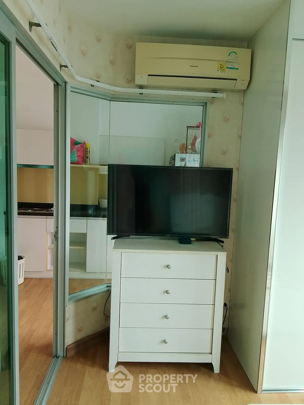 Cozy corner unit with modern TV setup and air conditioning, featuring a glimpse of a stylish kitchen.