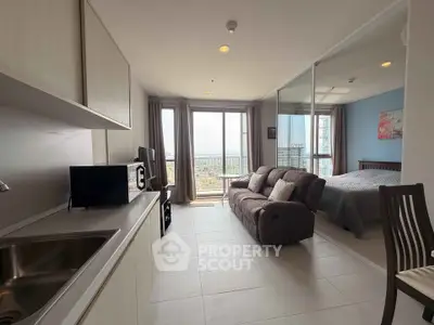 Modern open-plan living room with kitchen and bedroom, featuring large windows and a cozy sofa.