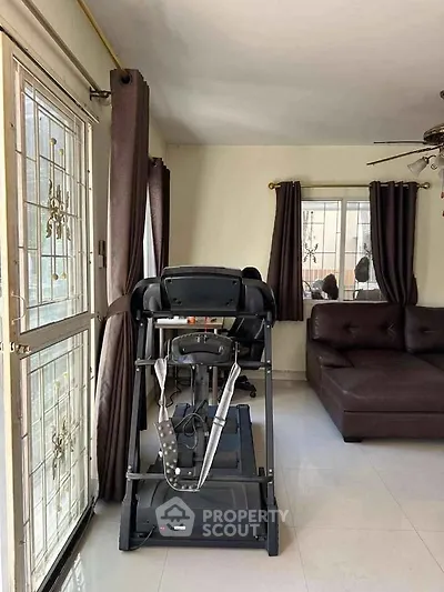 Spacious living room with treadmill and modern sofa, ample natural light through large windows.