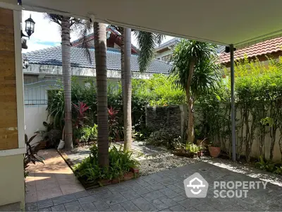 Charming garden patio with lush greenery and stone pathway, perfect for outdoor relaxation.