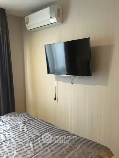 Modern bedroom with wall-mounted TV and air conditioning unit, featuring sleek design and cozy ambiance.