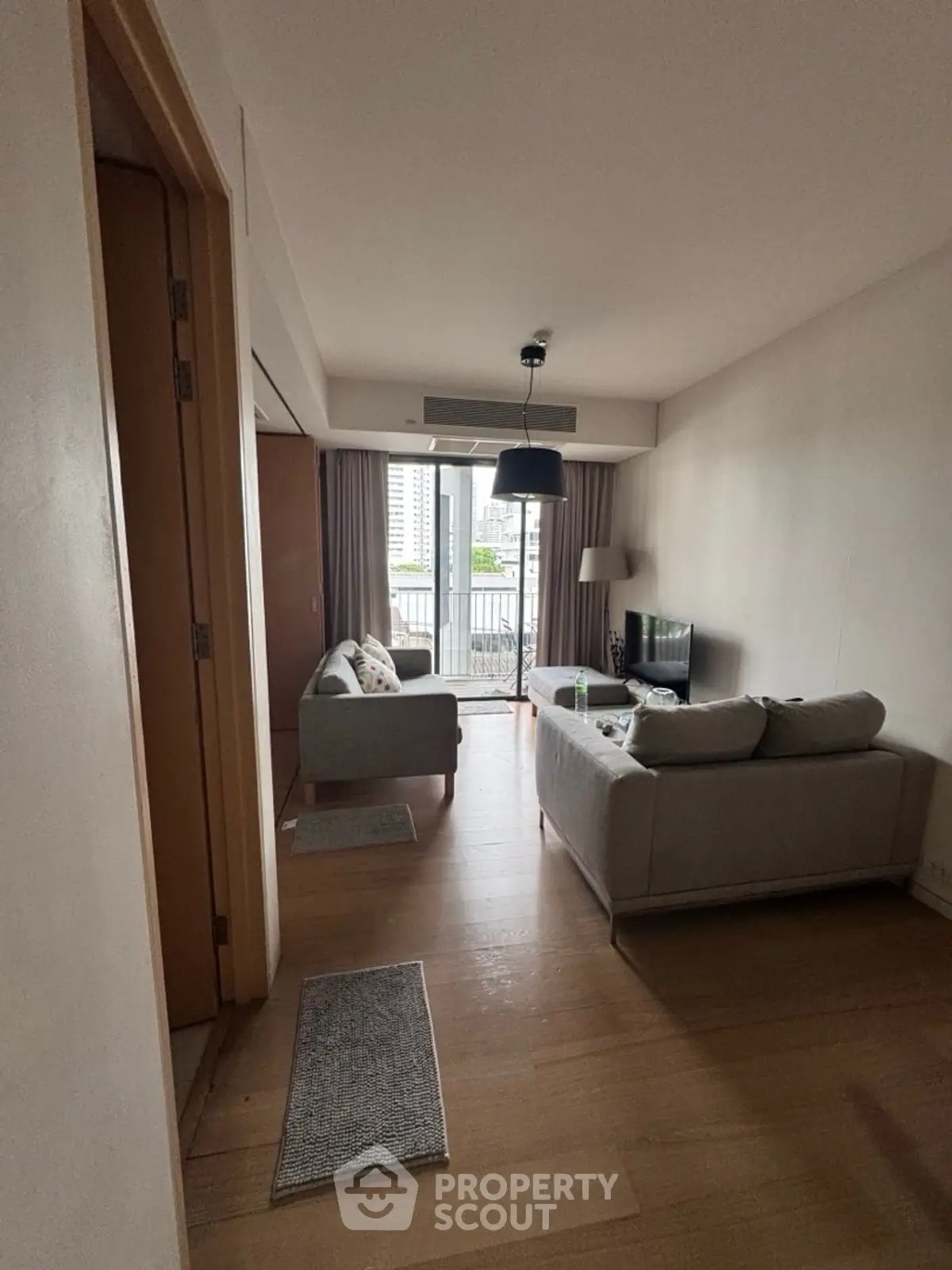 Modern living room with balcony view, cozy seating, and natural light in urban apartment.