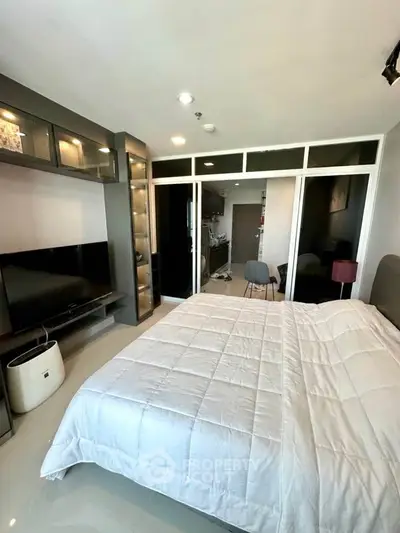 Modern bedroom with sleek design, featuring a large bed, built-in TV, and glass partition leading to a study area.