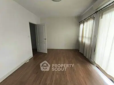 Spacious empty room with wooden flooring and large windows, perfect for customization.