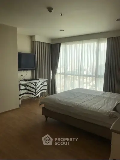Spacious bedroom with large window and modern decor in a high-rise apartment.