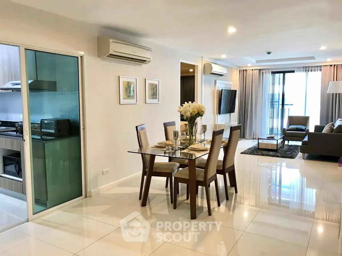 Spacious modern living room with dining area and glass-enclosed kitchen in luxury apartment.