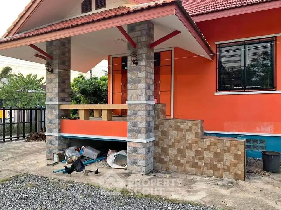 Charming orange house with tiled porch and stone columns, perfect for cozy living.