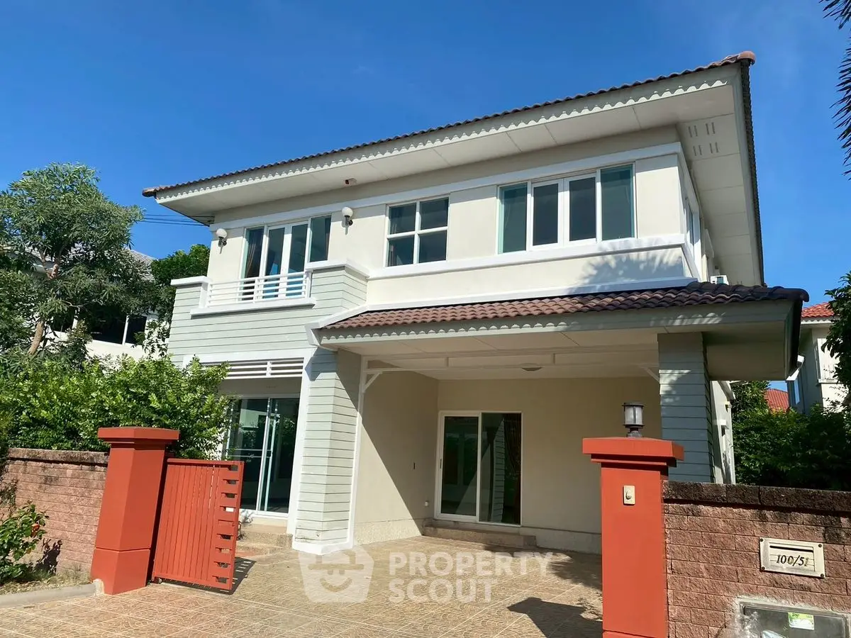 Charming two-story house with red gate and tiled roof in sunny neighborhood