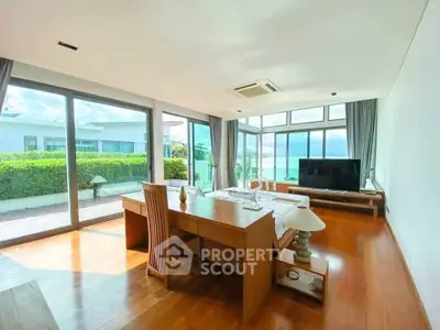 Spacious living room with large windows and ocean view, featuring modern furniture and wooden flooring.