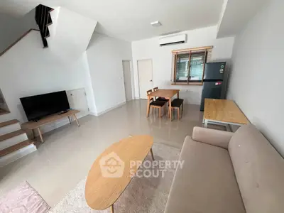 Modern living room with sleek furniture and open layout, featuring a cozy sofa, dining area, and staircase.