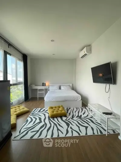 Modern bedroom with large window, stylish rug, and wall-mounted TV in a bright apartment.