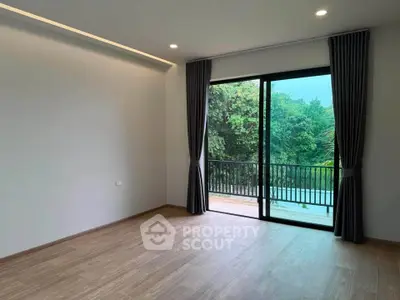 Spacious room with large window and balcony overlooking lush greenery, perfect for relaxation.
