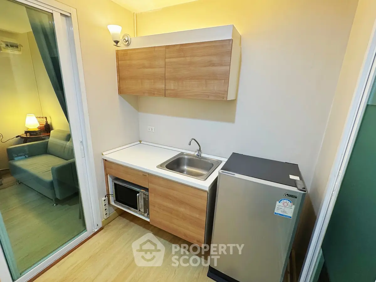 Compact kitchen with modern appliances and wooden cabinetry in cozy apartment.