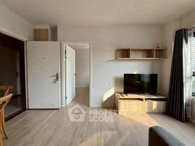 Modern living room with wooden flooring, TV unit, and natural light.