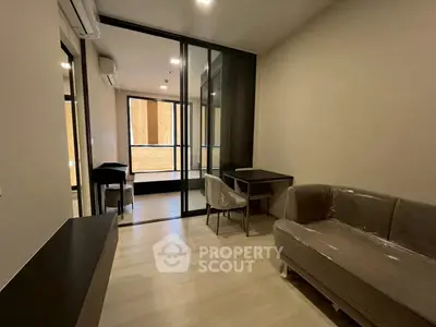 Modern living room with sleek furniture and glass partition leading to a balcony.
