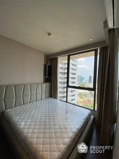 Modern bedroom with large window offering city view in high-rise apartment.