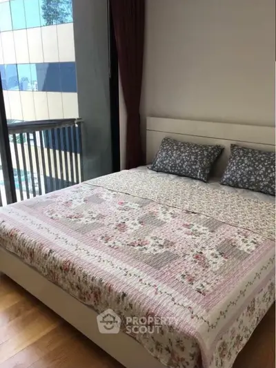 Cozy bedroom with floral bedding and large window offering natural light and city view.