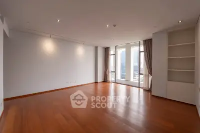 Spacious empty living room with wooden flooring and large windows offering city views.
