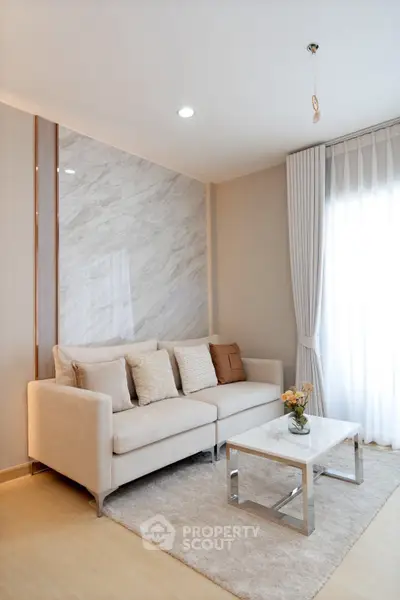 Elegant living room with modern sofa, marble accent wall, and natural light from large window.