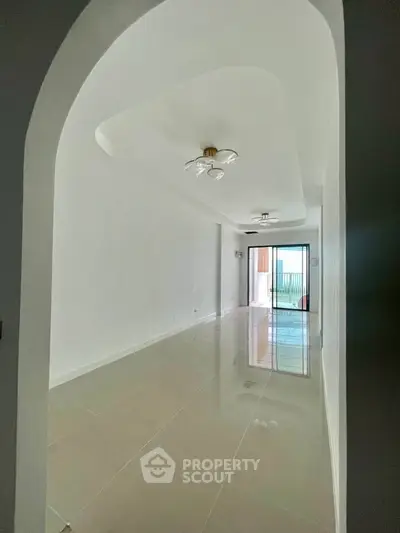 Spacious modern living room with glossy tiled floors and elegant lighting, leading to a balcony with natural light.