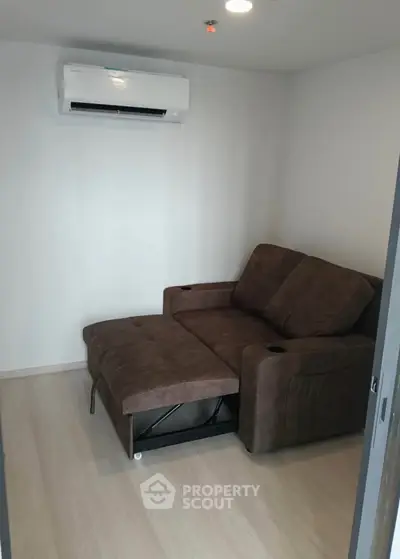 Cozy small living room with brown recliner sofa and wall-mounted air conditioner.