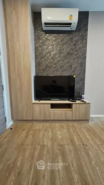 Modern living room with wooden flooring, stylish TV unit, and air conditioning.