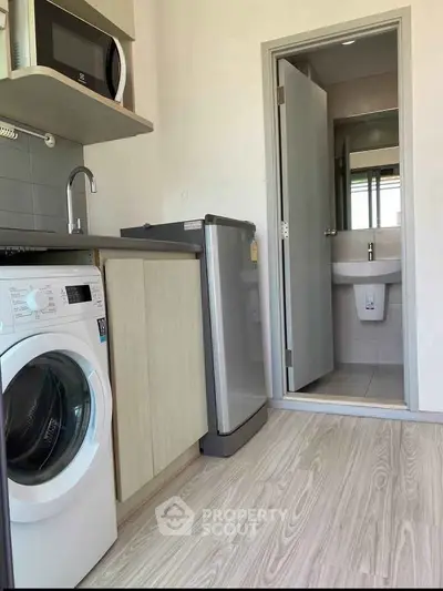 Compact kitchen with washing machine, microwave, and bathroom access in modern apartment.