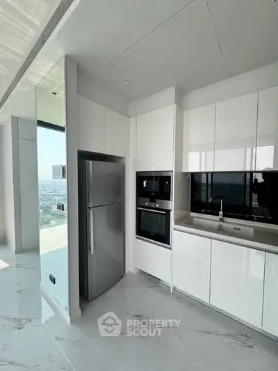 Modern kitchen with sleek white cabinetry and stainless steel appliances in a high-rise apartment.