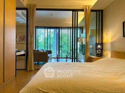 Spacious bedroom with sliding glass doors leading to a bright living area and lush garden view.