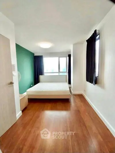 Spacious bedroom with wooden flooring and large windows for natural light.