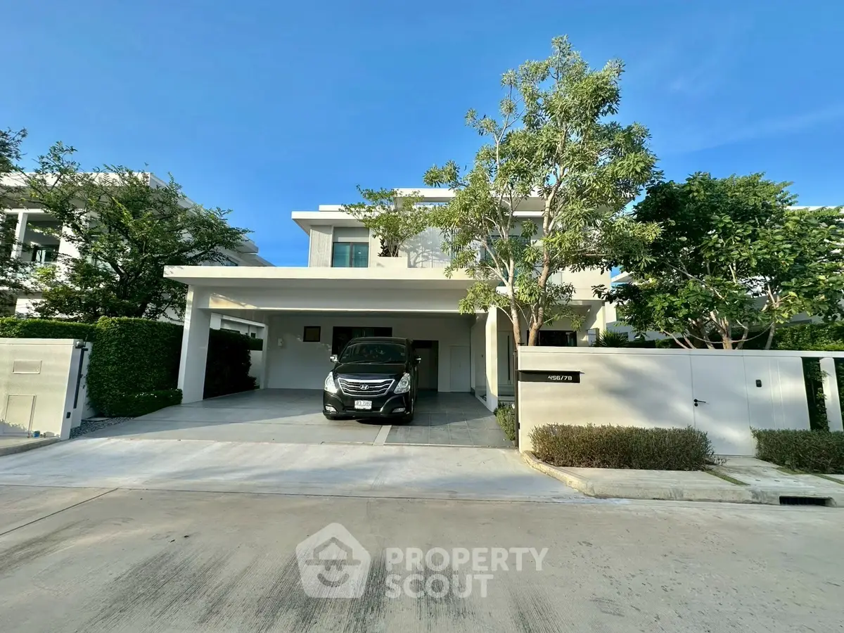 Modern two-story house with driveway and car parked, surrounded by lush greenery.