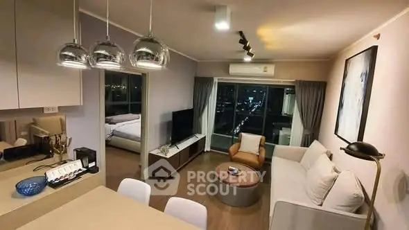 Modern living room with open kitchen and city view, featuring stylish lighting and cozy furnishings.