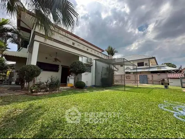 Spacious backyard with lush lawn and modern house exterior under cloudy sky.