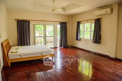 Spacious bedroom with wooden flooring and large windows offering natural light.