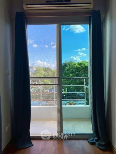 Charming balcony view from a cozy interior with lush greenery and blue skies.