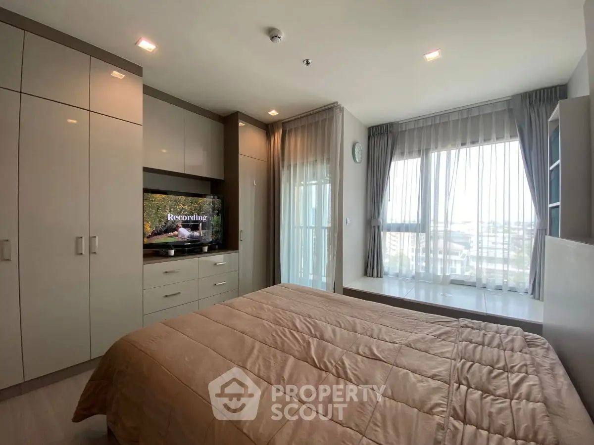 Modern bedroom with built-in wardrobe and large window offering city views.