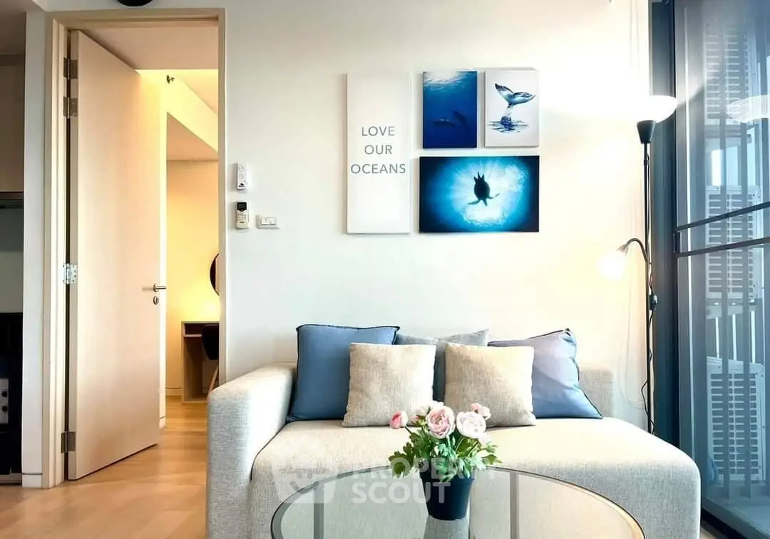 Modern living room with stylish decor and ocean-themed artwork, featuring a cozy sofa and glass coffee table.