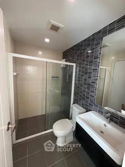 Modern bathroom with glass shower and sleek black tile accent wall.