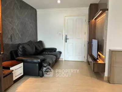 Modern living room with sleek black leather sofa and wall-mounted TV unit, featuring stylish decor and ample natural light.