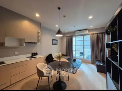 Modern living room with open kitchen and balcony view, featuring stylish furniture and ample natural light.