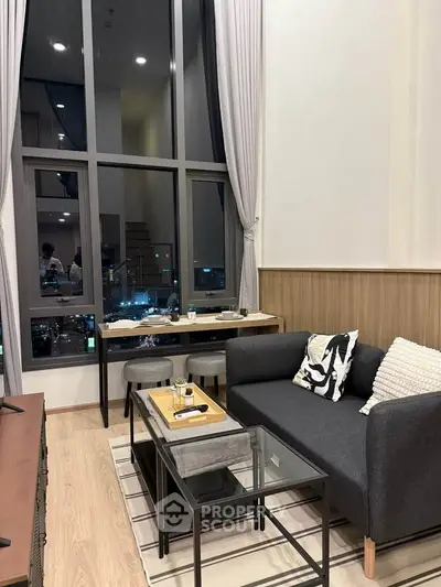 Modern living room with high ceilings and large windows offering city views, featuring stylish furniture and decor.