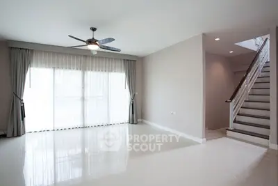 Spacious living room with modern ceiling fan and natural light near staircase