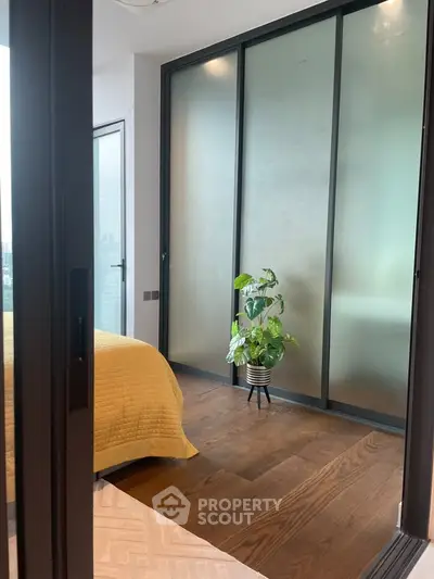 Modern bedroom with frosted glass sliding doors and wooden flooring, featuring a cozy yellow bedspread and a potted plant.
