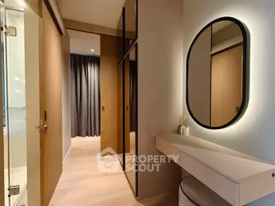 Modern bedroom with sleek vanity and mirrored closet doors, featuring elegant lighting and minimalist decor.