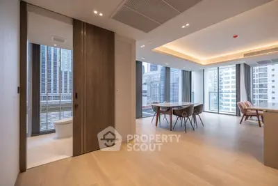 Modern open-plan living and dining area with city view, featuring sleek wooden flooring and large windows.