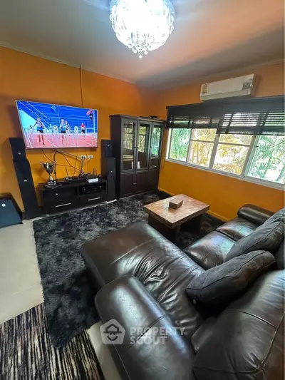 Cozy living room with leather sofa, large TV, and elegant chandelier, perfect for relaxation and entertainment.