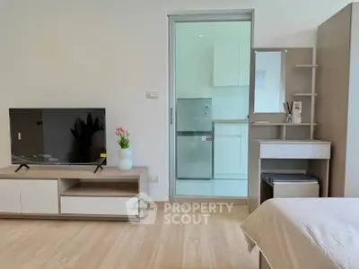 Modern studio apartment with sleek TV stand and cozy bed, featuring a compact kitchen area.