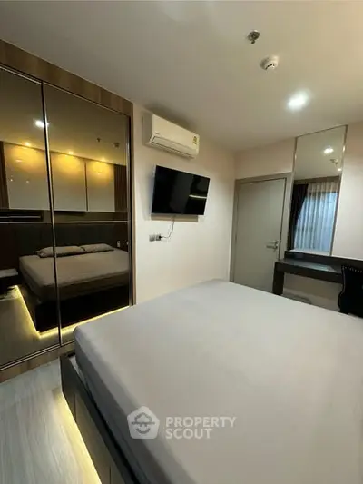 Modern bedroom with mirrored wardrobe and wall-mounted TV in stylish apartment.