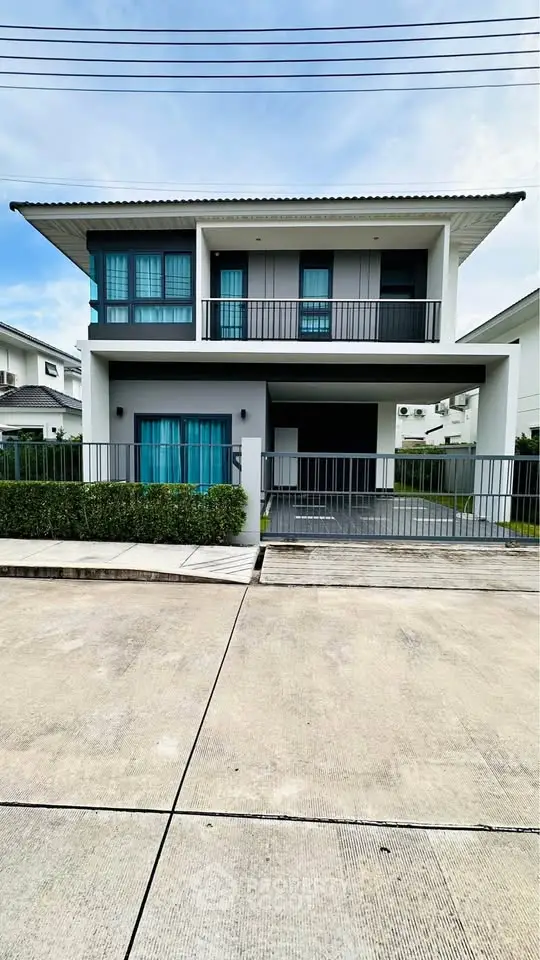 Modern two-story house with balcony and driveway in a suburban neighborhood.